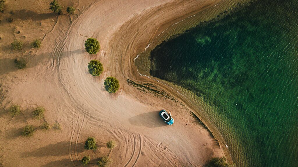 Aerial Photography of Vehicle Parked on Beach Near Bushes